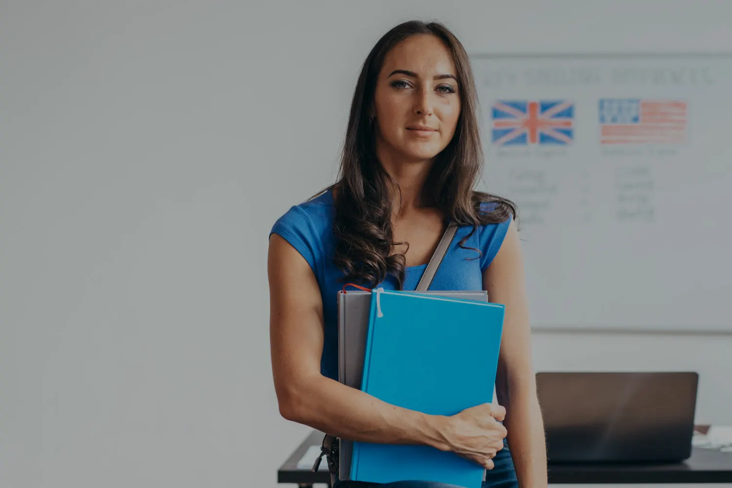 Docente con cartelline davanti a una lavagna con le bandiere inglese e americana